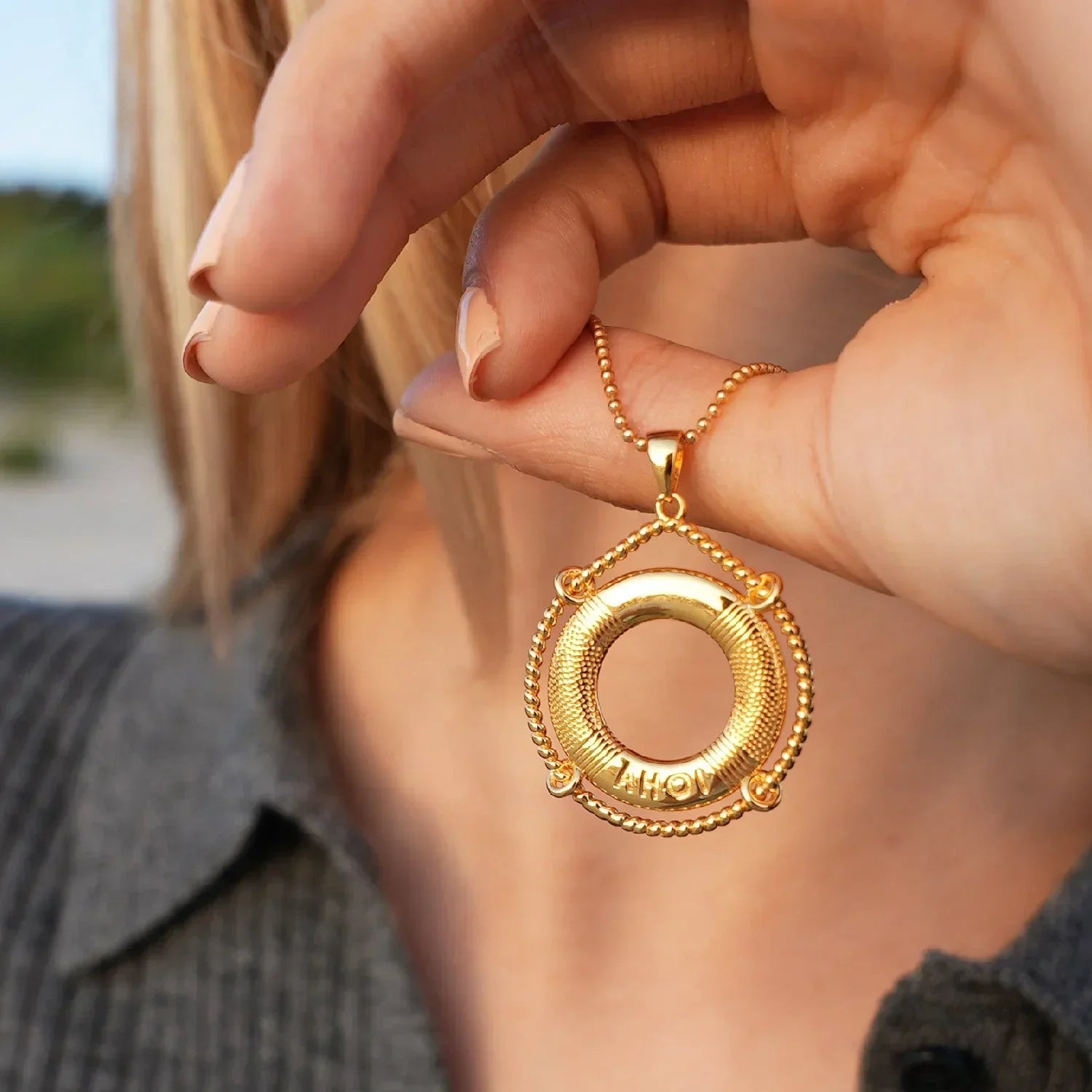 Goldene Halskette mit maritimem Rettungsring-Anhänger und AHOI-Gravur am Hals einer Frau