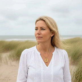 Frau mit goldener Rettungsring-Kette am Strand, maritimer Schmuck vor Dünen und Meer