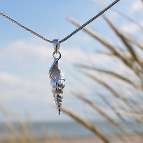 Silberne Muschel-Anhänger Kette am Strand vor blauem Himmel, maritimer Schmuck