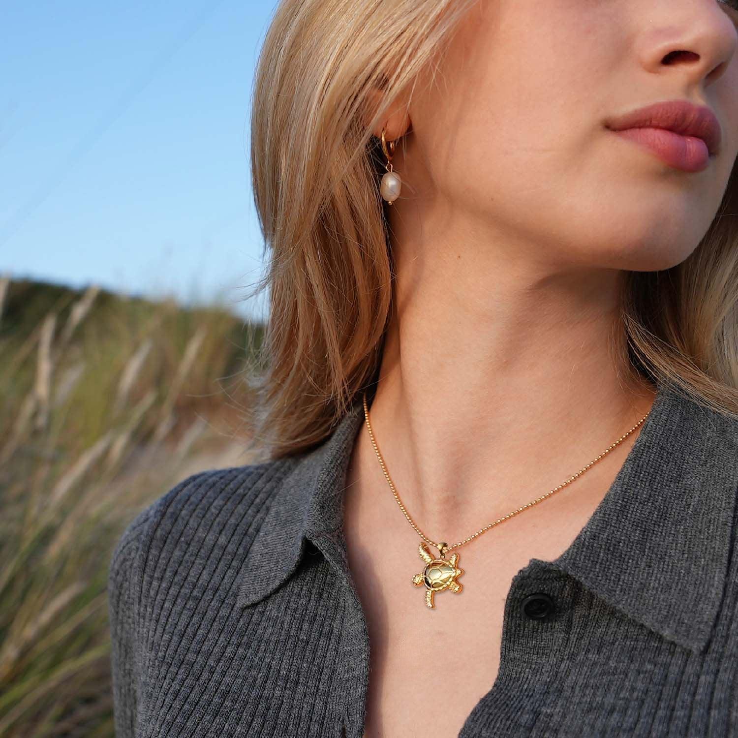 Frau mit goldener Schildkrötenkette und Perlenohrring am Strand, maritimer Schmuck