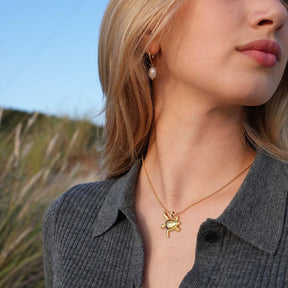 Frau mit goldener Schildkrötenkette und Perlenohrring am Strand, maritimer Schmuck