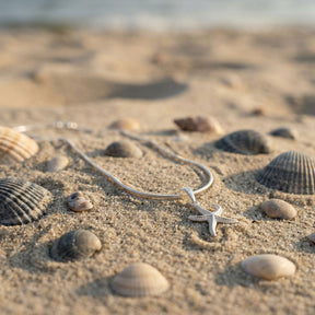 Silberne Seestern-Kette auf Sand mit Muscheln am Strand, maritimer Schmuck