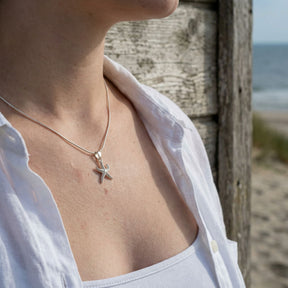 Frau trägt silberne Seestern-Kette am Strand, maritimer Schmuck, Sommer-Outfit