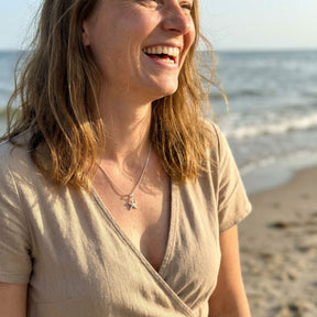 Frau am Strand trägt Silberkette mit Seestern-Anhänger, maritimer Schmuck, Meer im Hintergrund