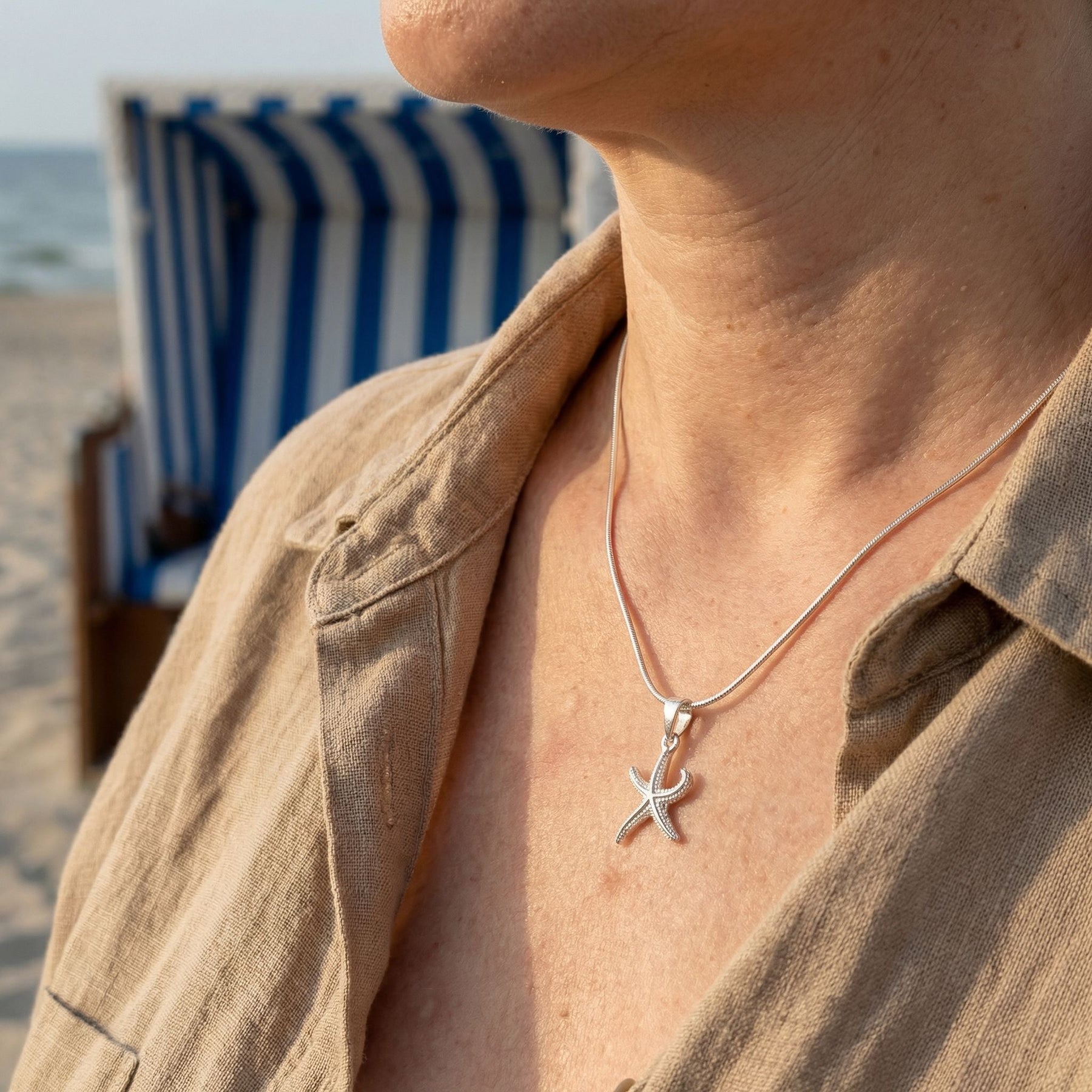 Frau trägt eine silberne Seestern-Kette am Strand mit Strandkorb im Hintergrund