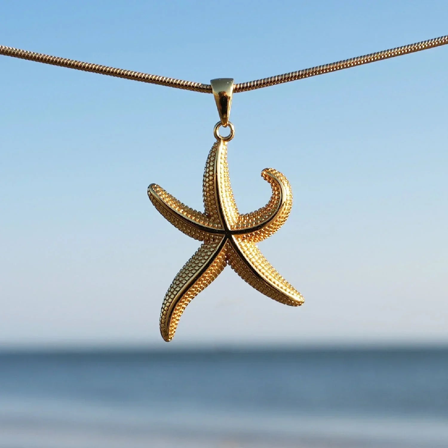 Goldene Seestern-Kette als maritimer Schmuck vor blauem Himmel und Meer