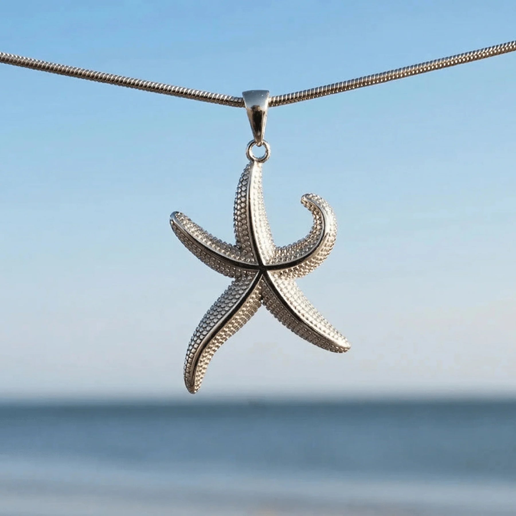 Silberner Seestern Anhänger, maritimer Schmuck, Kette vor Meereshintergrund