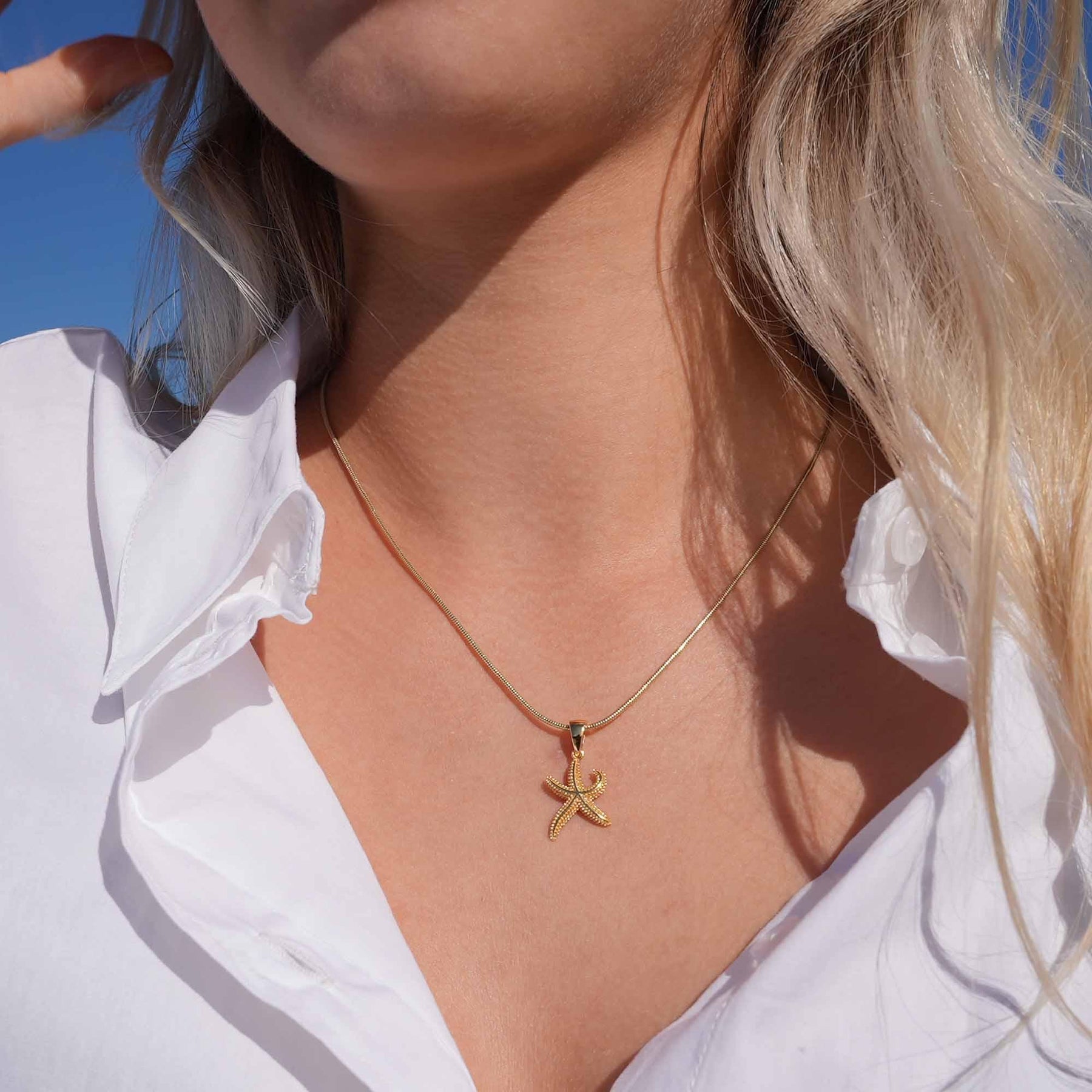 Goldene Seestern Halskette an Frau mit weißer Bluse, maritimer Schmuck im Sonnenlicht