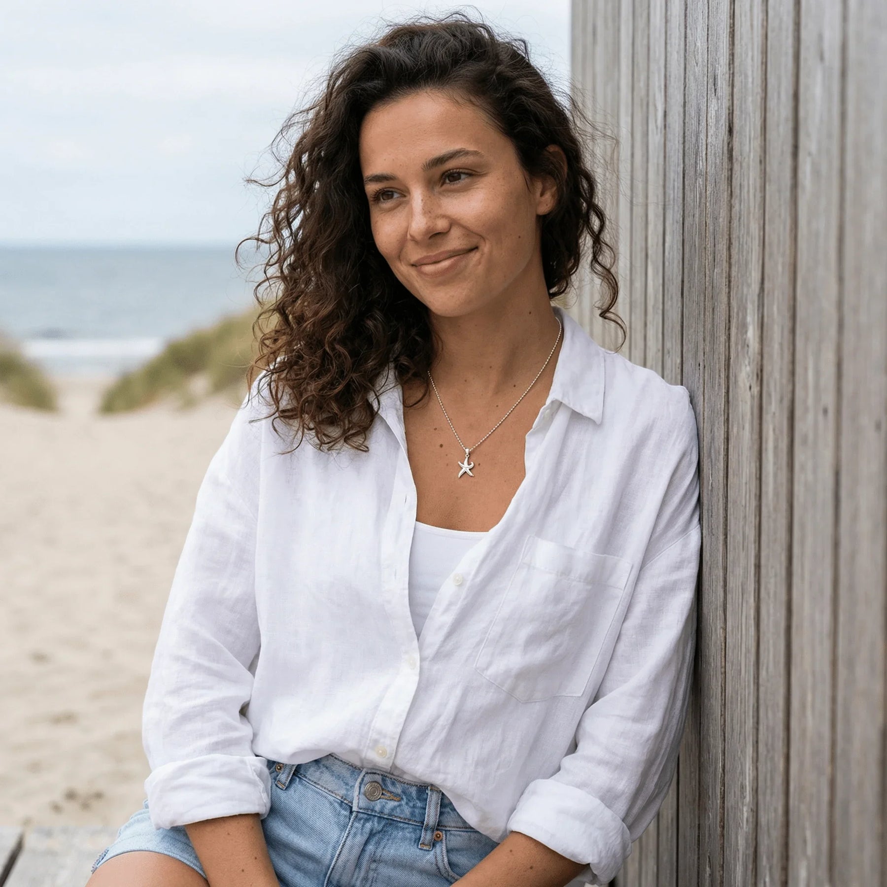 Frau am Strand mit weißem Hemd und silberner Seestern-Kette, maritimer Schmuck Look