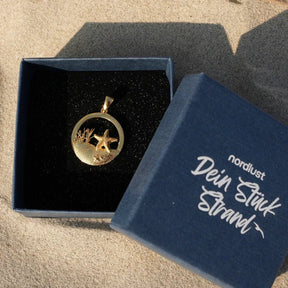 Goldener Seestern-Anhänger rund mit Dünenmotiv in Schmuckschachtel am Strand