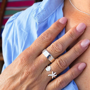 Silberner Ring mit Seestern und Muschel am Finger, maritimer Schmuck, Nahaufnahme
