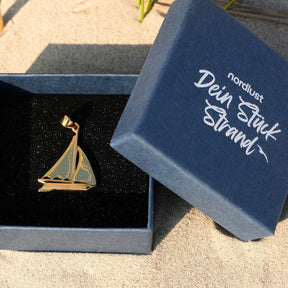 Goldener Segelboot Anhänger in Geschenkbox auf Sand, maritimer Schmuck