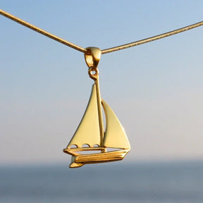Goldener Segelboot Anhänger an Kette vor maritimem Hintergrund, maritimer Schmuck