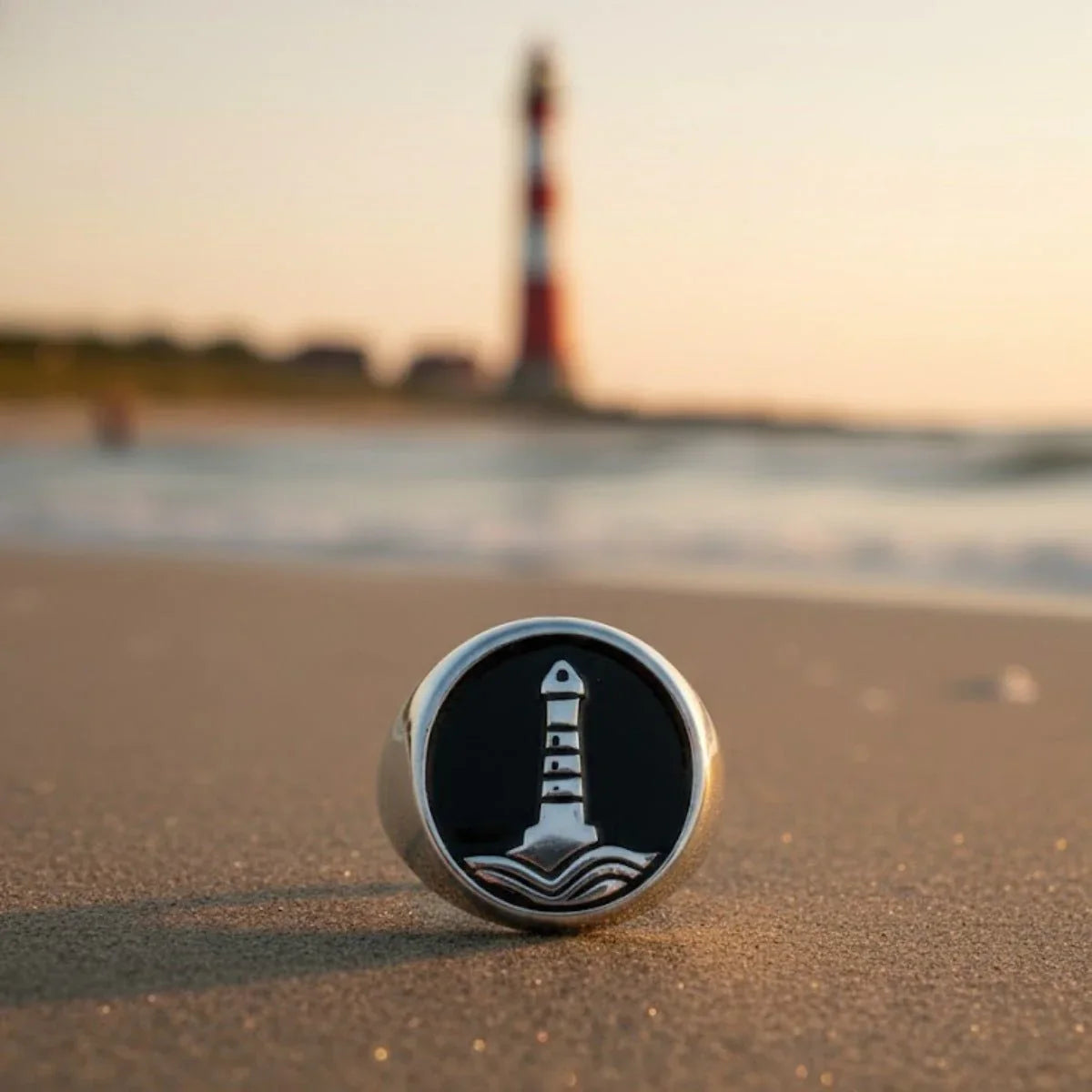 Silberner Siegelring mit Leuchtturm-Motiv am Strand im Sonnenuntergang