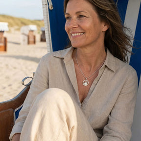Frau im Strandkorb am Strand mit maritimer Kette und beigem Leinenhemd