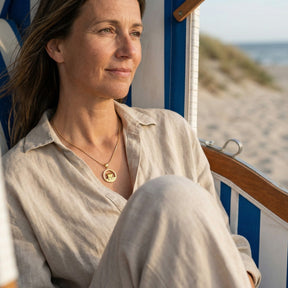 Frau mit goldener Strandkorb-Kette sitzt entspannt im Strandkorb am Meer