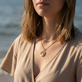 Frau am Strand mit goldener Kette und Anhänger mit Strandkorb-Motiv, Meereskulisse