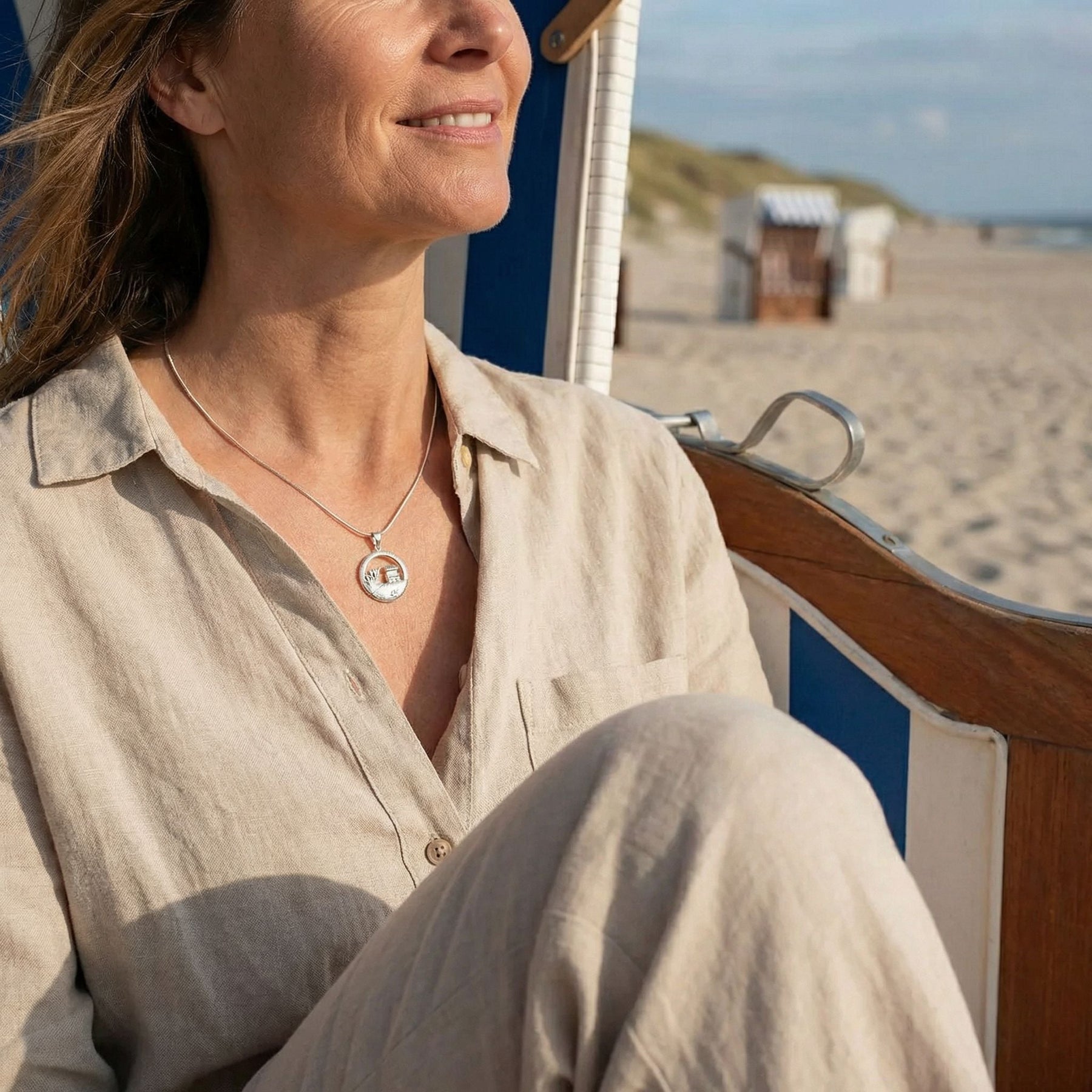 Frau im Strandkorb am Strand mit maritimer Kette, Dünen und Meer im Hintergrund