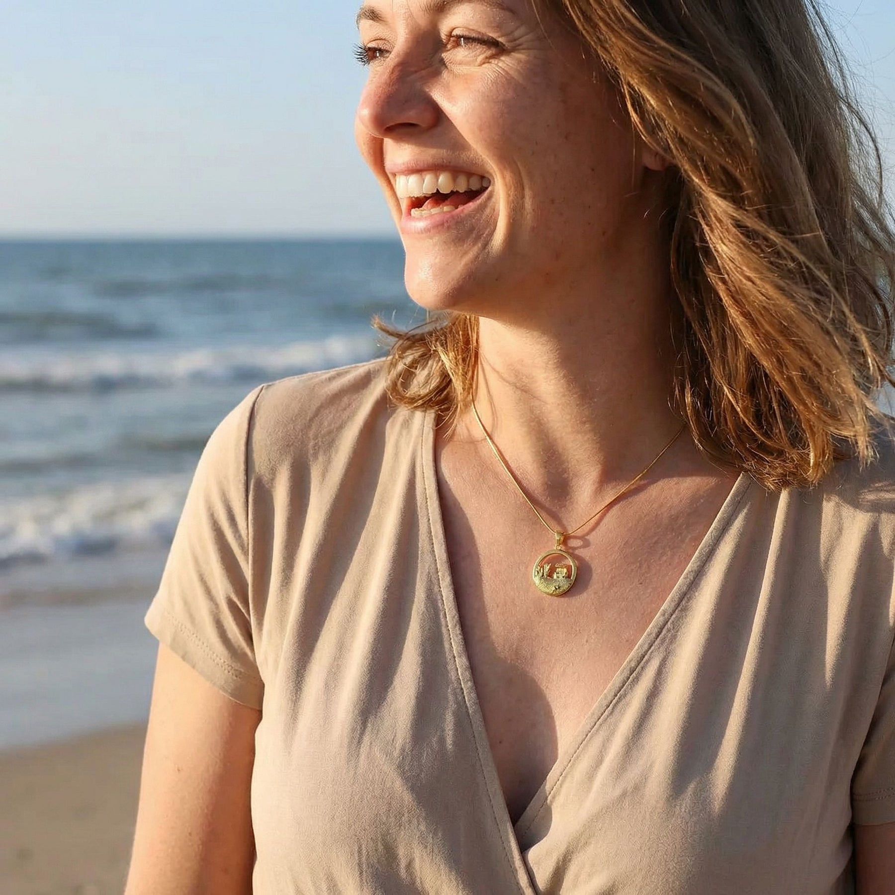 Lachende Frau am Strand mit goldener Kette und Anhänger, Meereswellen im Hintergrund
