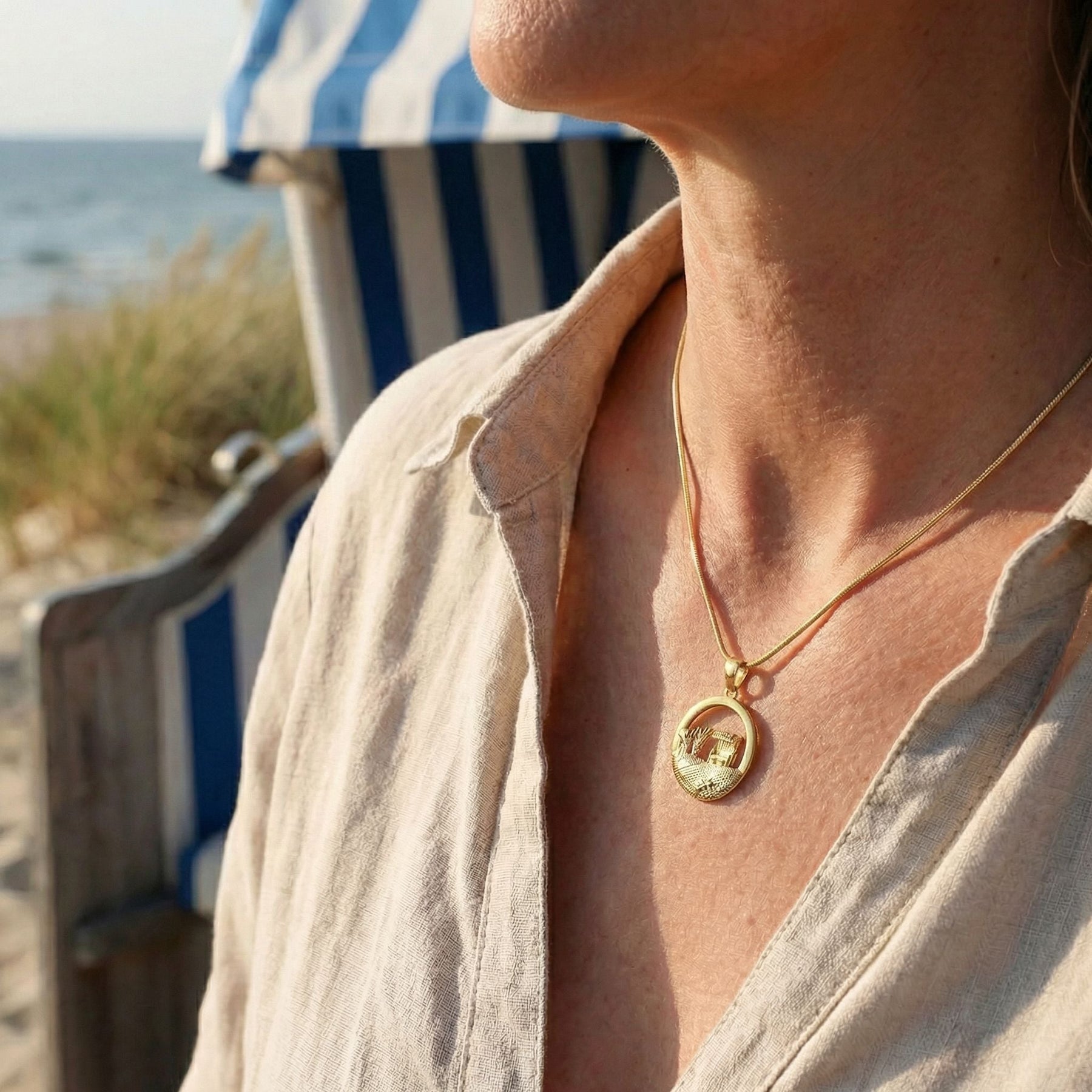 Goldene Kette mit Strandkorb-Anhänger, getragen am Strand mit maritimer Kulisse