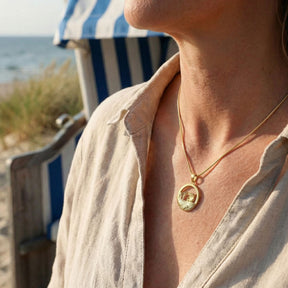 Goldene Kette mit Strandkorb-Anhänger, getragen am Strand mit maritimer Kulisse