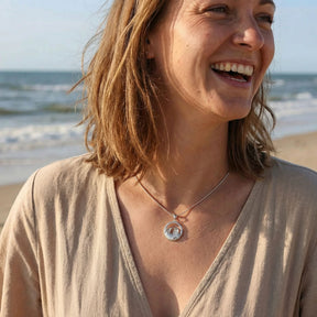 Frau am Strand mit silberner Kette, rundem Anhänger mit Strandkorb-Motiv, maritimer Schmuck