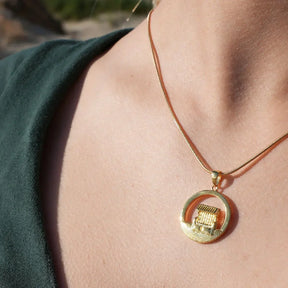 Goldene Halskette mit rundem Anhänger und Strandkorb-Motiv am Hals einer Frau, maritimer Schmuck