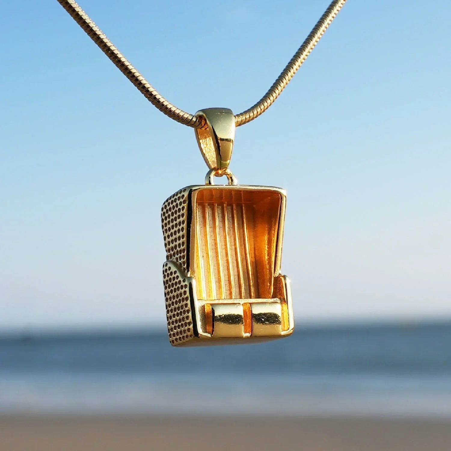 Goldener Strandkorb Anhänger maritimer Schmuck am Meer vor blauem Himmel