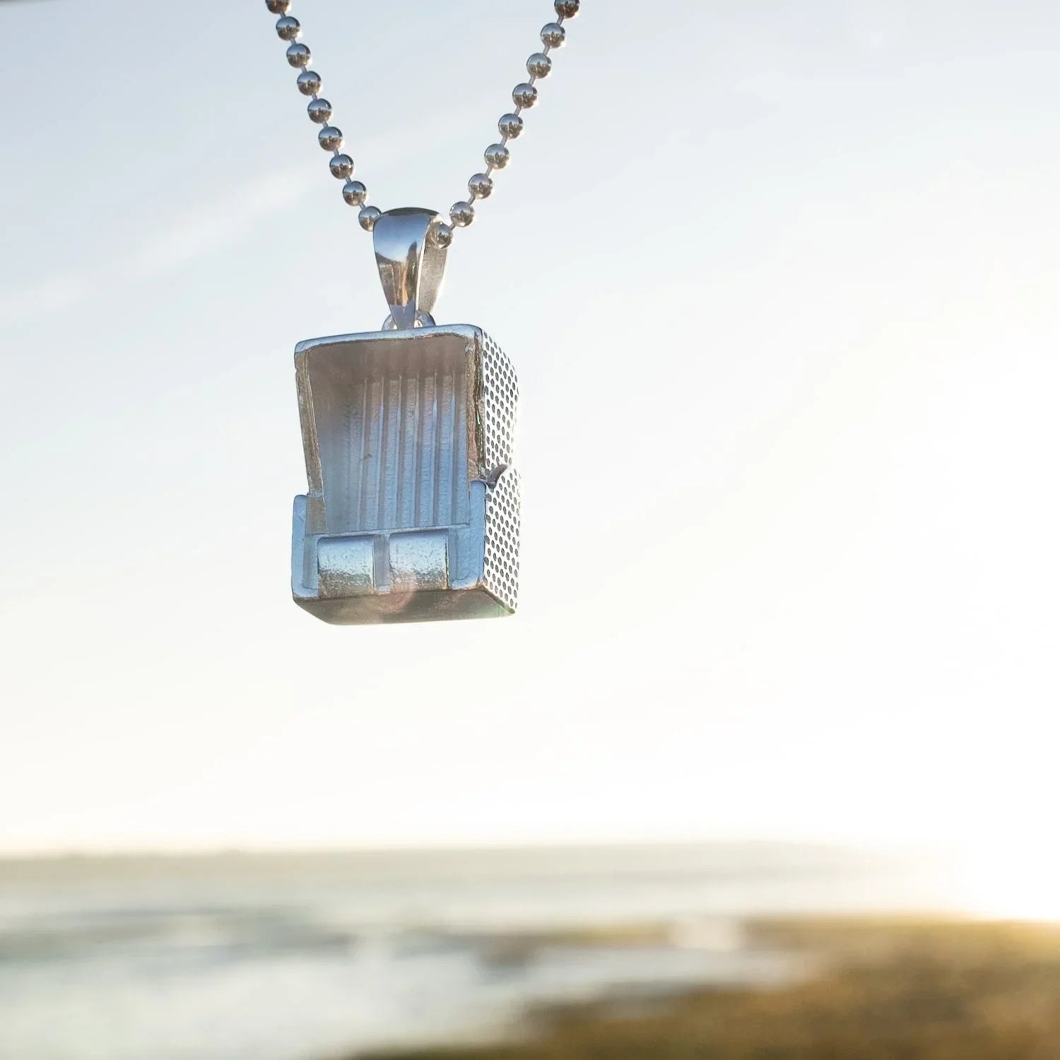 Strandkorb Anhänger aus Silber an Kette, maritimer Schmuck am Meer im Sonnenlicht