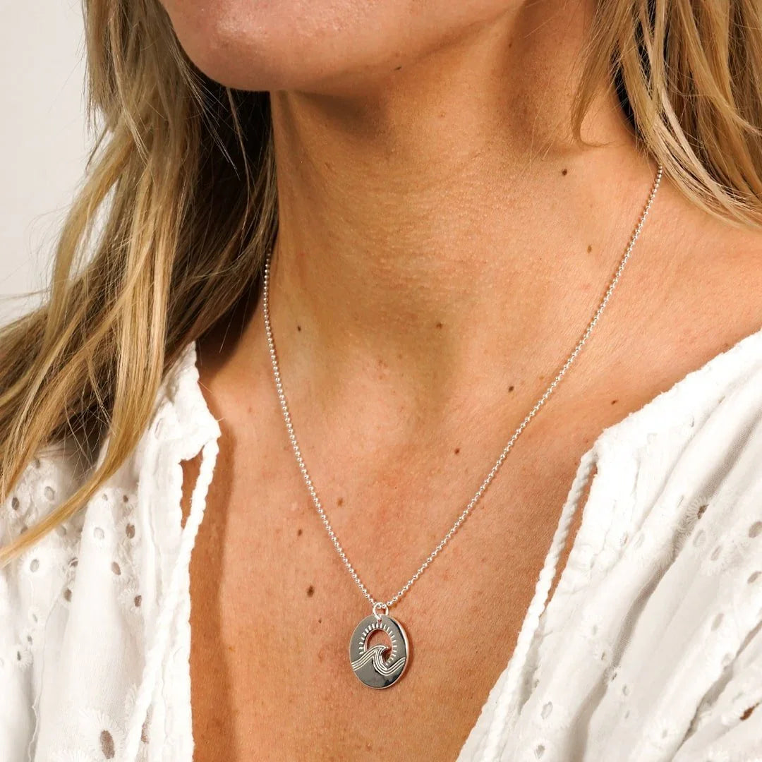 Silberne Kette mit rundem Wellen-Anhänger, maritimer Schmuck auf weißer Bluse getragen