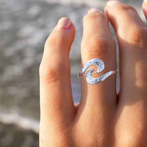 Silberner Wellenring am Finger vor unscharfem Meeres-Hintergrund, maritimer Schmuck