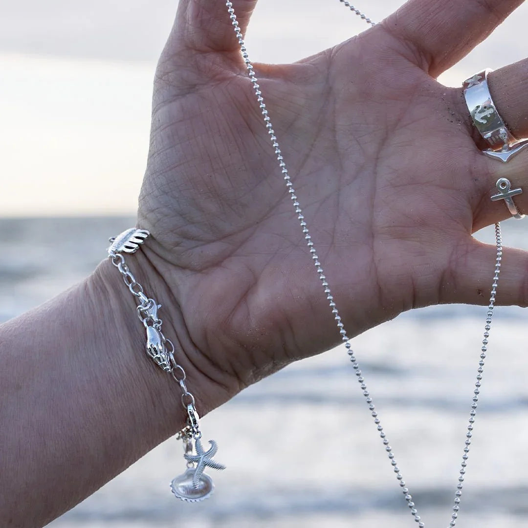 Detailreiches Silberarmband mit Wellhornschnecke und maritimen Anhängern am Strand